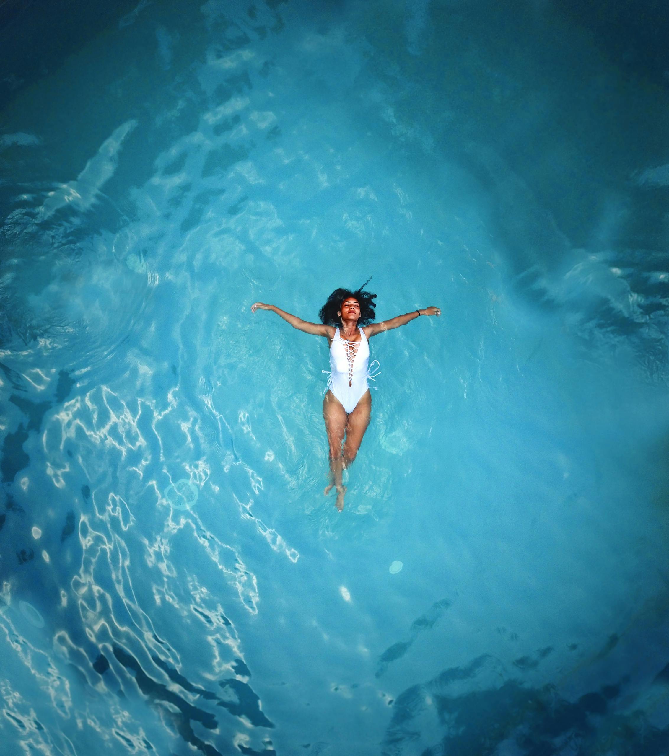 Female in white bathing suit floating peacefully in the middle of a large pool filled with crystal clear blue water