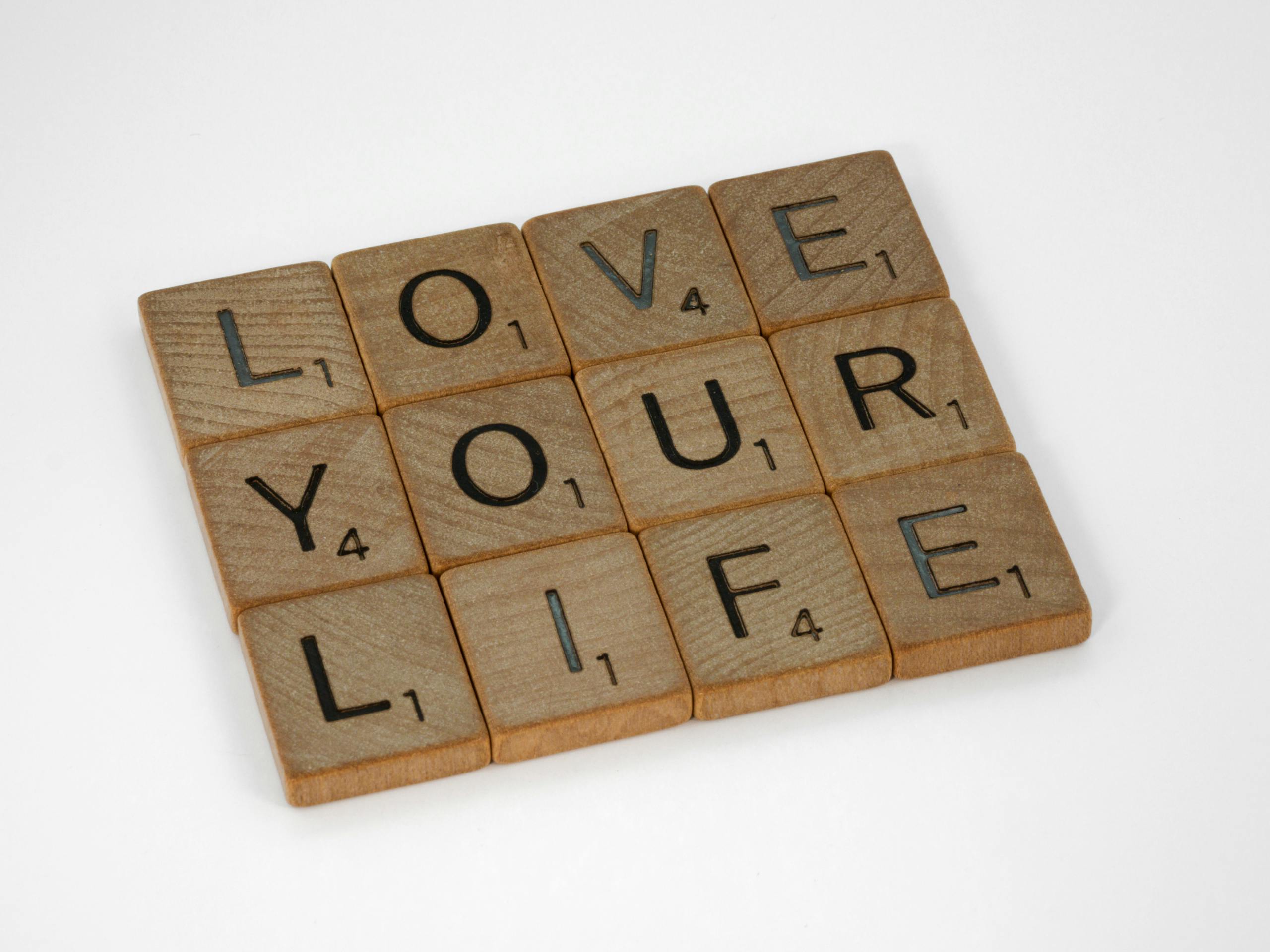 scrabble tiles arranged to spell love your life against a white background conveying a positive message