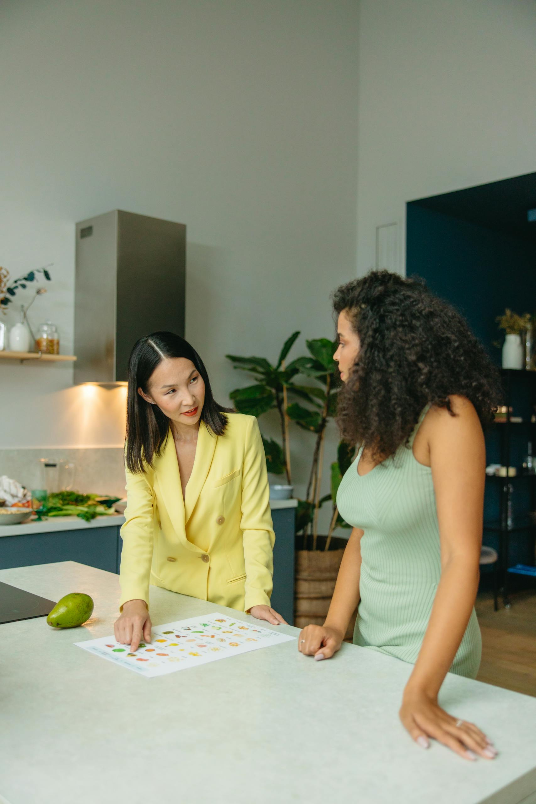 Two women discussing healthy eating in a stylish kitchen setting with fresh vegetables