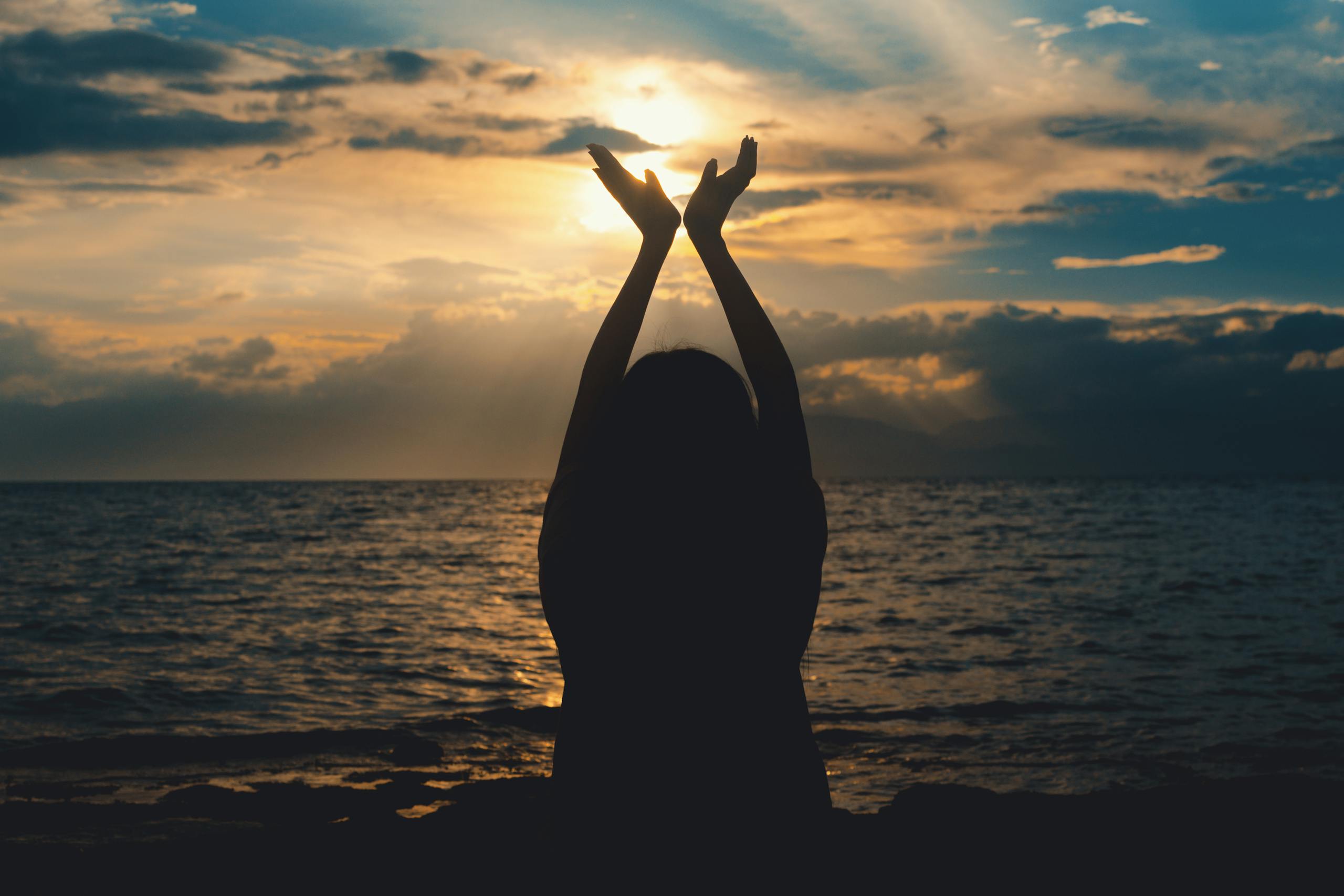 a-silhouetted-figure-raises-hands-towards-the-setting-sun-over-a-serene-ocean-view